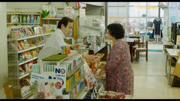 フードセンター日吉内の食品スーパーのレジ前で、女性客と話す店員（兄）。
